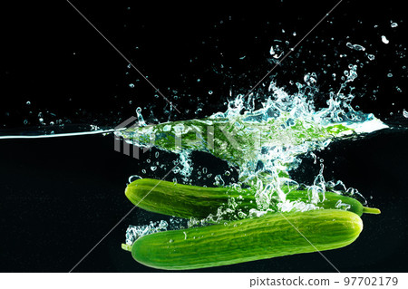 Cucumbers falling into the water with a splash againsty black background 97702179
