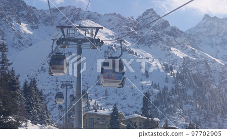 Lift cabins in a mountain ski resort. The movement of ski lifts in a snowy winter mountain in sunny day. Kazahstan 97702905