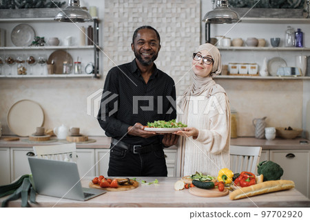 Attractive african american man and muslim young woman holding bowl with healthy salad 97702920