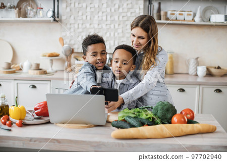 Pretty young mother and two children sons preparing salad with fresh vegetables 97702940