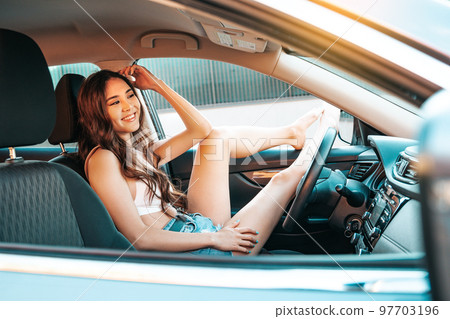 Beautiful asian ethnicity girl resting behind the wheel of a parked car with her legs out the window. 97703196