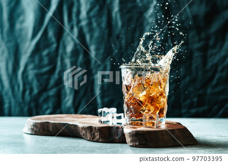 Splash of whiskey from the glass with ice on the table. Splash of whiskey from the glass with ice on the table. 97703395