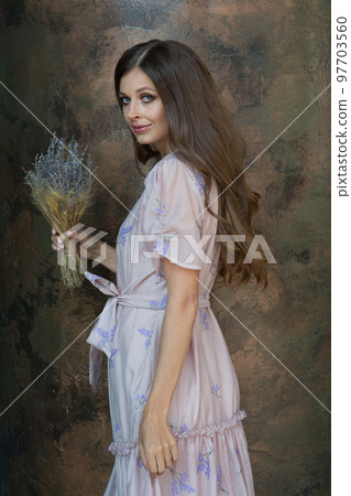 A woman with a half-turn smile looks directly into the camera with dried lavender flowers. The brunette poses with a bouquet of dried flowers against a brown marble wall. High quality photo A woman with a half-turn smile looks directly into the camera with dried lavender flowers. The brunette poses with a bouquet of dried flowers against a brown marble wall. High quality photo 97703560