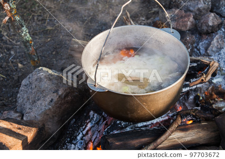 Cauldron with boiling tourist soup hangs over an open fire Cauldron with boiling tourist soup hangs over an open fire 97703672