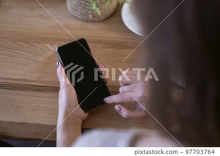 Smart phone in female hands with blank black screen. Phone against on wooden table background. Smart phone in female hands with blank black screen. Phone against on wooden table background. 97703764