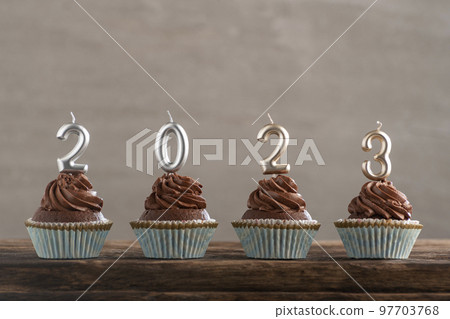 Chocolate cupcakes with buttercream frosting with silver 2023 candles on wooden table on light gray concrete background. Chocolate cupcakes with buttercream frosting with silver 2023 candles on wooden table on light gray concrete background. 97703768