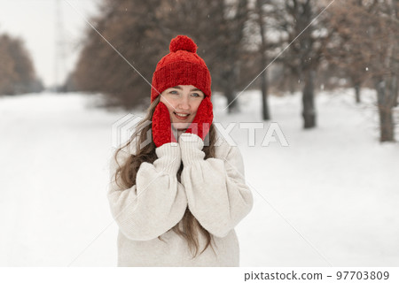 Portrait of pretty smiling girl in red knitted hat and mittens and woolen sweater on alley in winter park. Woman outdoor 97703809
