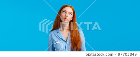 Be unusual. Carefree and funny cute redhead teenage girl fooling around showing roommate funny faces during sleepover in pyjama, tilt head, squinting and showing fish face, blue background 97703849