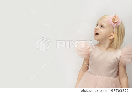 Girl in beautiful pink dress surprised looking up . Blonde-haired girl isolated on white background. Space for text 97703872