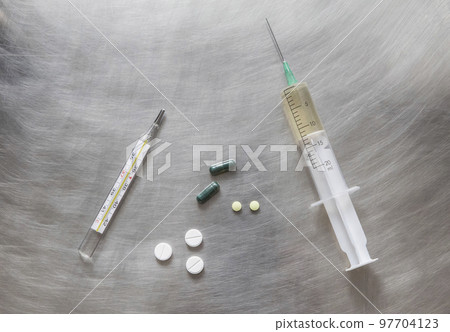 syringe, thermometer and pills lie on a metal medical table 97704123