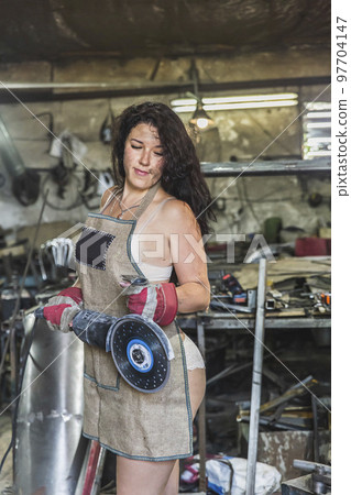 girl blacksmith holding a angle grinder in the workshop 97704147
