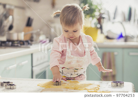 Adorable baby in an apron makes cookies from dough in the kitchen Adorable baby in an apron makes cookies from dough in the kitchen 97704253