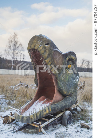 Abandoned huge head of decorative dinosaur on winter lawn Abandoned huge head of decorative dinosaur on winter lawn 97704257