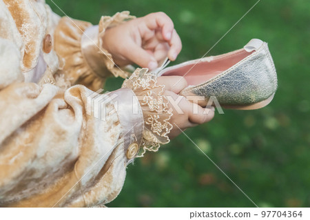 baby in princess costume holding small golden shoes in hands 97704364