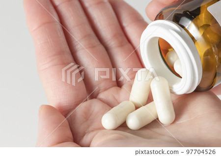A woman holds pills in her hand, pours capsules with painkillers into her hand to get rid of pain. Taking pills or antibiotics, treating various diseases. A woman holds pills in her hand, pours capsules with painkillers into her hand to get rid of pain. Taking pills or antibiotics, treating various diseases. 97704526
