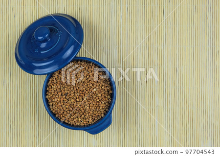 Buckwheat in in blue bowl on a straw background. Vegetarian organic product. Vintage view. Top view. Copy space. 97704543