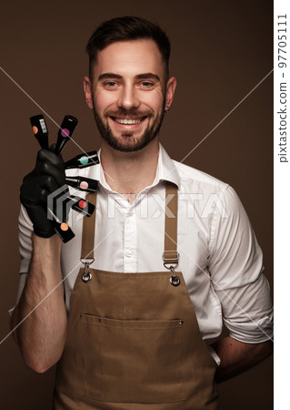 Manicur master man in working form with bottles of nail polish in hand. Nail photo content 97705111