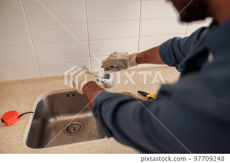 Close up of male plumber repair sink faucet at kitchen. Good quality plumbing company service Close up of male plumber repair sink faucet at kitchen. Good quality plumbing company service 97709248