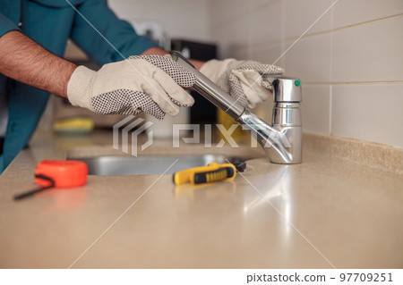 Close up of male plumber repair sink faucet at kitchen. Good quality plumbing company service Close up of male plumber repair sink faucet at kitchen. Good quality plumbing company service 97709251