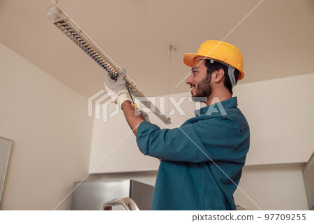 Smiling Professional electrician worker in uniform is installing electric lamps light in kitchen 97709255