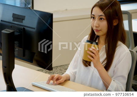 Working woman looking at a computer screen at work and drinking coffee 97710654