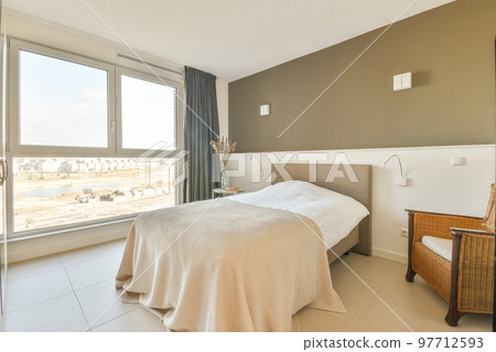 Retro bedside table with books and lamp located near comfortable bed and shelf with decorations against window in modern bedroom 97712593