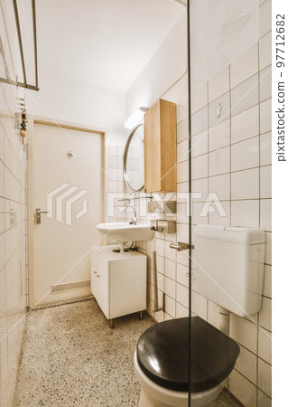 Interior of narrow restroom with sink and wall hung toilet with white walls and checkered floor 97712682