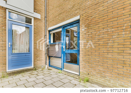 The front view of a brick building with signs, pavement and wooden doors lead to the apartment The front view of a brick building with signs, pavement and wooden doors lead to the apartment 97712716
