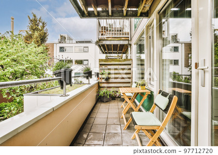 Narrow brick balcony with metal railings, wooden chair and door 97712720
