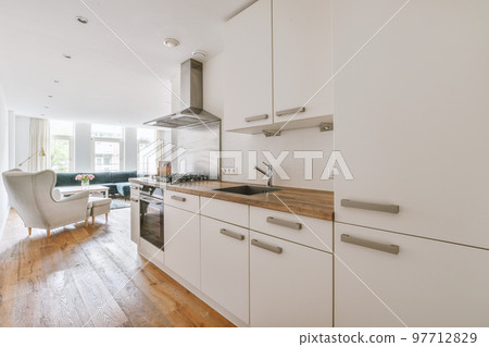 Fragment of interior of light narrow home kitchen with minimalist style white furniture with sink and stove 97712829
