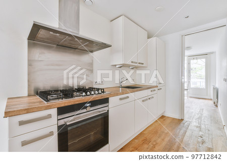 Fragment of interior of light narrow home kitchen with minimalist style white furniture with sink and stove Fragment of interior of light narrow home kitchen with minimalist style white furniture with sink and stove 97712842