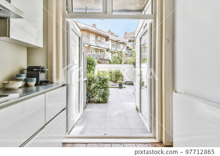 Fragment of interior of light narrow home kitchen with minimalist style white furniture with sink and stove Fragment of interior of light narrow home kitchen with minimalist style white furniture with sink and stove 97712865