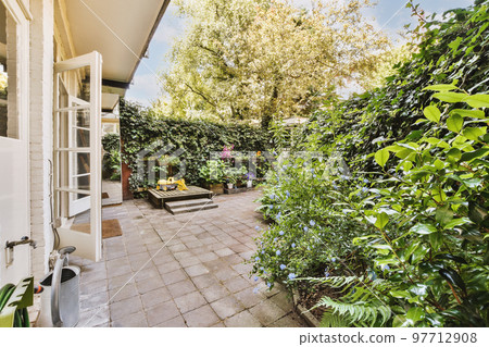 Neat paved patio with sitting area and small garden near wooden fence 97712908