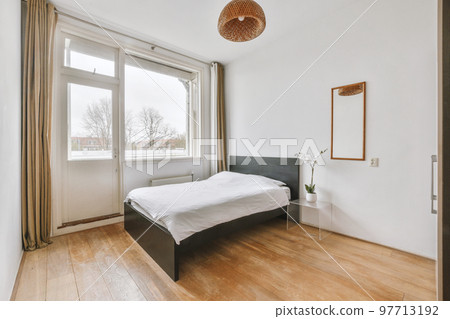 Home interior design of bedroom with bed and wooden wardrobe placed in corner near window in modern apartment 97713192