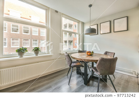 Table with chairs and flowers located near lounge area and kitchen in spacious room of contemporary apartment 97713242