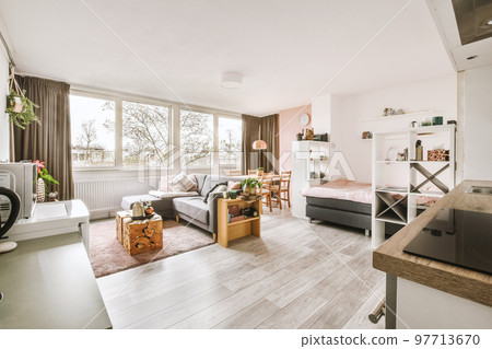 Table with chairs and flowers located near lounge area and kitchen in spacious room of contemporary apartment 97713670