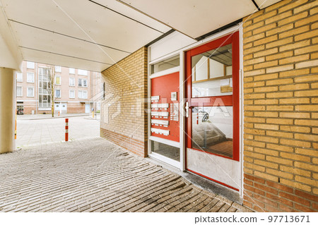 The front view of a brick building with signs, cars, pavement and wooden doors lead to the apartment The front view of a brick building with signs, cars, pavement and wooden doors lead to the apartment 97713671