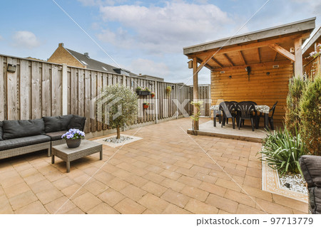 Neat paved patio with sitting area and small garden near wooden fence 97713779