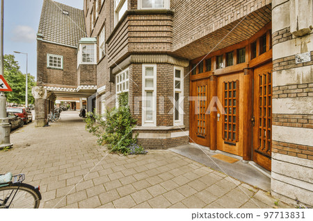 The front view of a brick building with signs, pavement and wooden doors lead to the apartment 97713831