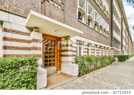 The front view of a brick building with signs, pavement and wooden doors lead to the apartment 97713833