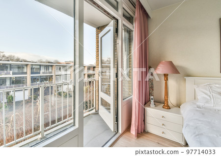 Comfortable bed located near balcony door with curtains in cozy light bedroom at home 97714033