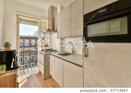 Light small home kitchen with wide window furnished with cupboards and shelves with appliances in modern urban apartment Light small home kitchen with wide window furnished with cupboards and shelves with appliances in modern urban apartment 97714067