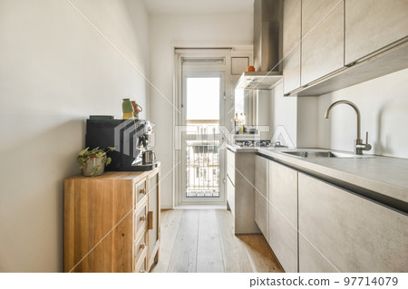Light small home kitchen with wide window furnished with cupboards and shelves with appliances in modern urban apartment 97714079