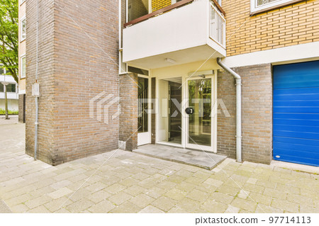 The front view of a brick building with signs,pavement and wooden doors lead to the apartment The front view of a brick building with signs,pavement and wooden doors lead to the apartment 97714113