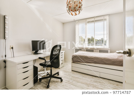 a bedroom with a bed, desk and computer monitor on the table in front of the window that looks out to the city 97714787