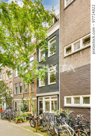 bikes parked on the side of a street in front of a building with many windows and plants growing out of it 97714822