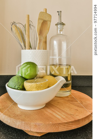some lemons and limes in a bowl on a wooden cutting board next to a bottle of olive oil some lemons and limes in a bowl on a wooden cutting board next to a bottle of olive oil 97714994