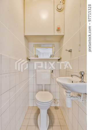a small bathroom with white tiles on the walls and floor, there is a mirror above the toilet in the corner a small bathroom with white tiles on the walls and floor, there is a mirror above the toilet in the corner 97715328