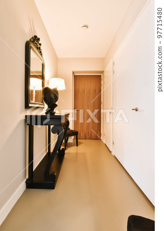 a hallway with a mirror on the wall and a black chair in the corner next to the door, there is a lamp a hallway with a mirror on the wall and a black chair in the corner next to the door, there is a lamp 97715480