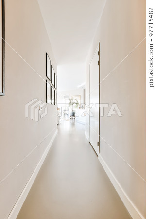 a long hallway with white walls and wood flooring the room is well lit by natural light from the windows a long hallway with white walls and wood flooring the room is well lit by natural light from the windows 97715482